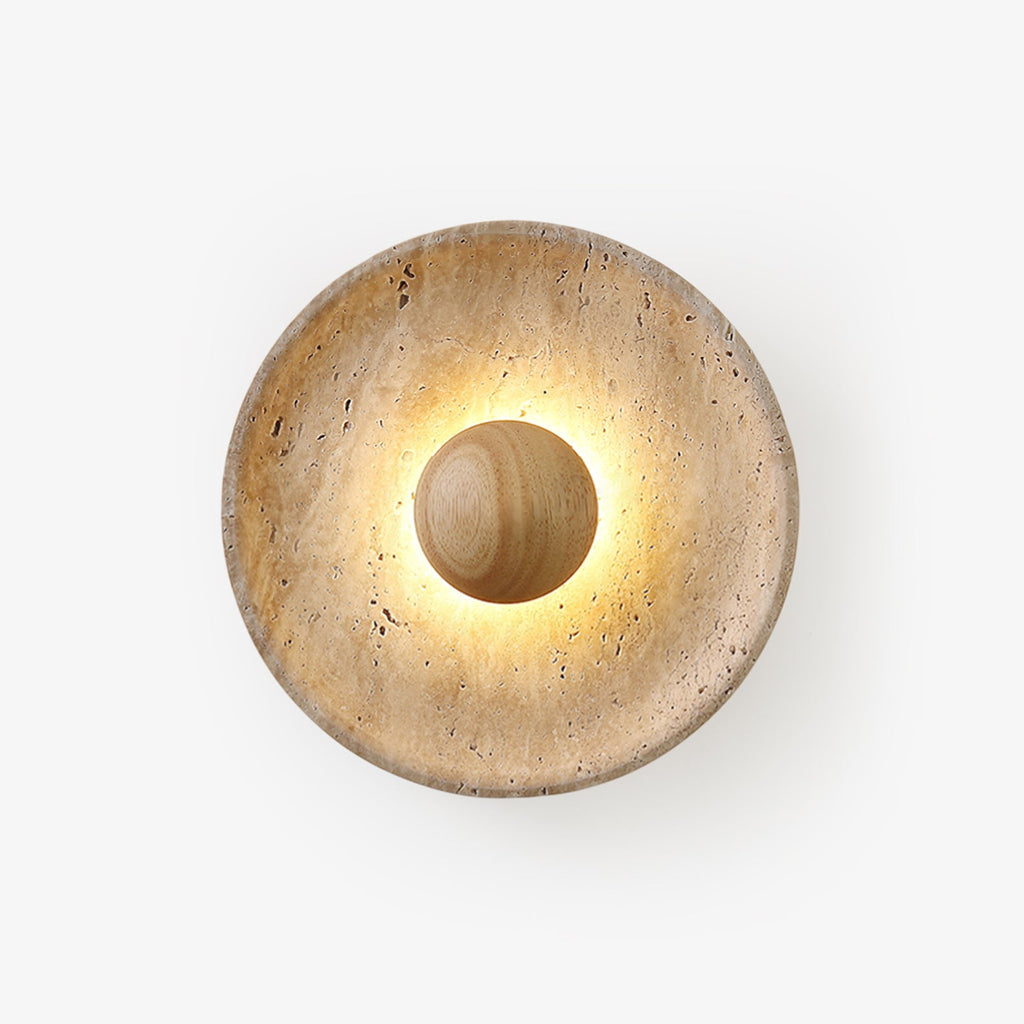 Round Clérachic travertine wall light lit on a white backdrop, with a pale wood dome at the centre and warm light glowing around it.