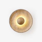 Round Clérachic travertine wall light lit on a white backdrop, with a pale wood dome at the centre and warm light glowing around it.
