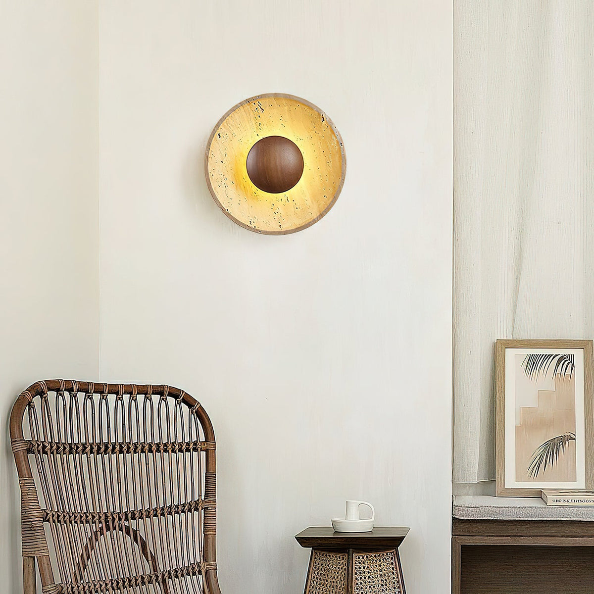 Clérachic round wall light in yellow travertine with a walnut centre dome, glowing above a rattan chair and a small framed print.