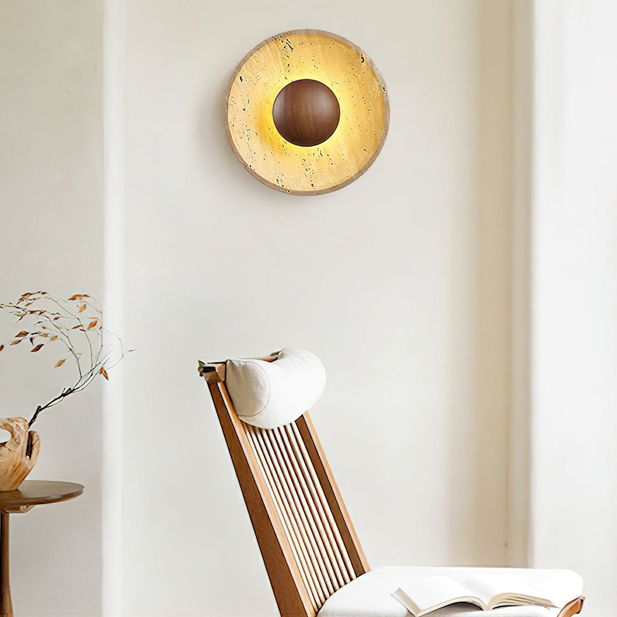 Lit Clérachic travertine wall light with a walnut dome high on a cream wall, above a slatted wooden chair with a cushion.