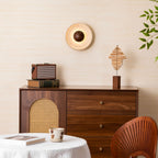Lit Clérachic travertine wall light with a walnut dome on a cream wall, above a walnut cabinet with a rattan door and a retro radio.