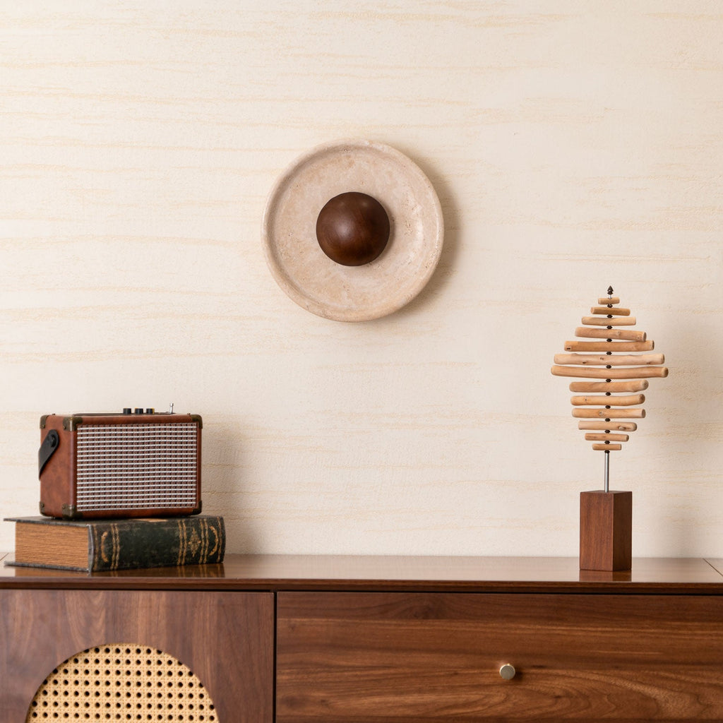 Closer view of the unlit Clérachic travertine wall light with its walnut dome, above a radio on a stack of books and a stepped wood sculpture.