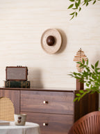 Unlit Clérachic travertine wall light with a walnut dome above a walnut sideboard with brass knobs, leaves in the lower right.