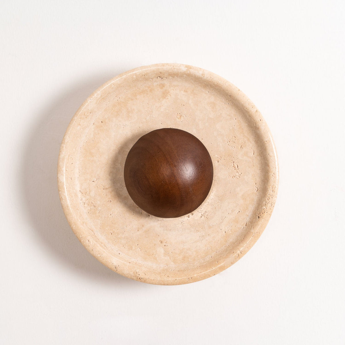 Close view of the unlit Clérachic travertine wall light on white, showing the raised stone rim, pale veining and a polished walnut dome.