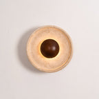 Lit Clérachic travertine wall light on a pale wall, with a stepped stone rim and a walnut dome with a soft halo of light behind it.