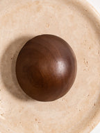 Close view of the walnut dome of this Clérachic wall light, its grain and the pitted yellow travertine around it.