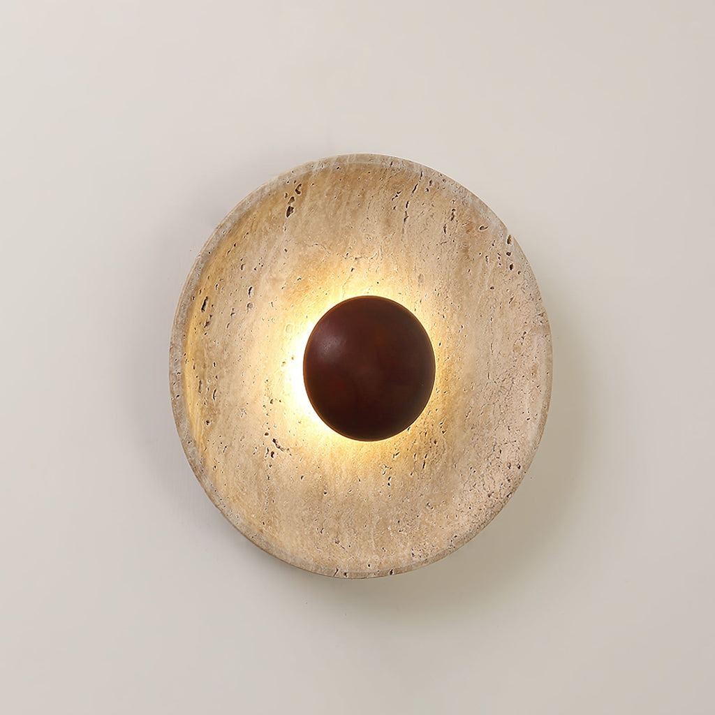 Clérachic wall light lit warm on a pale wall, with a shallow, veined travertine dish and a walnut dome at its centre.