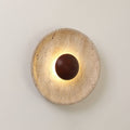 Clérachic wall light lit warm on a pale wall, with a shallow, veined travertine dish and a walnut dome at its centre.
