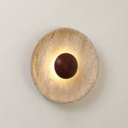 Clérachic wall light lit warm on a pale wall, with a shallow, veined travertine dish and a walnut dome at its centre.