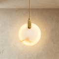 Clérachic round alabaster pendant glowing from within, hung from a braided brass-toned cord and bracket on limewash.