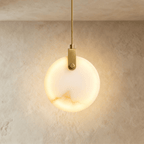 Clérachic round alabaster pendant glowing from within, hung from a braided brass-toned cord and bracket on limewash.