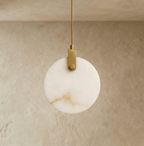 Clérachic round alabaster pendant switched off, showing its warm veining and a brushed brass-toned bracket on a braided cord.
