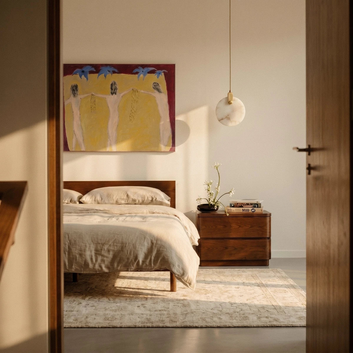 Clérachic round alabaster pendant hung beside a bed and walnut bedside chest, glowing softly against a cream wall.
