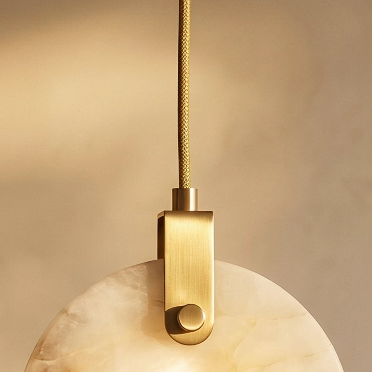 Clérachic close view of the brass-toned bracket, braided cord and cloudy alabaster disc of the pendant.