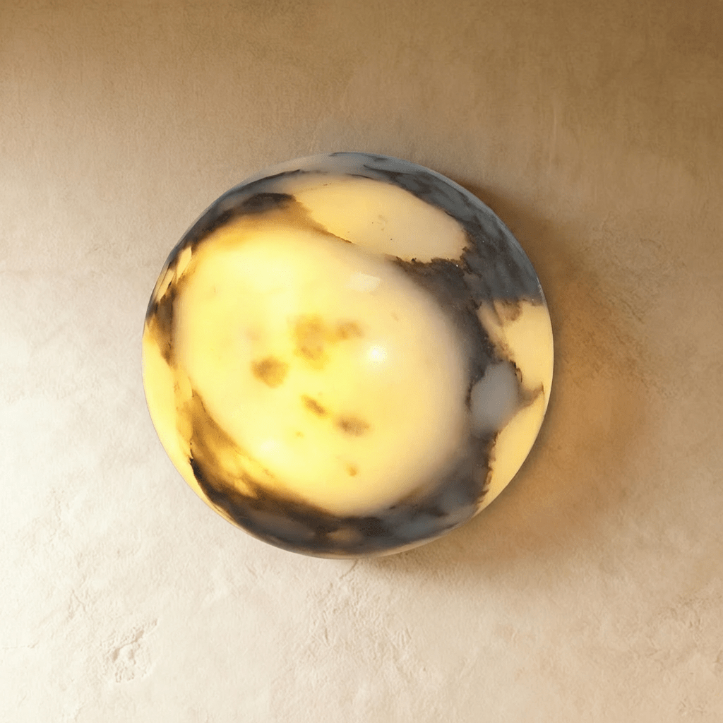 Clérachic wall lamp lit in close-up, its stone dome glowing warm through dark grey-black veining.