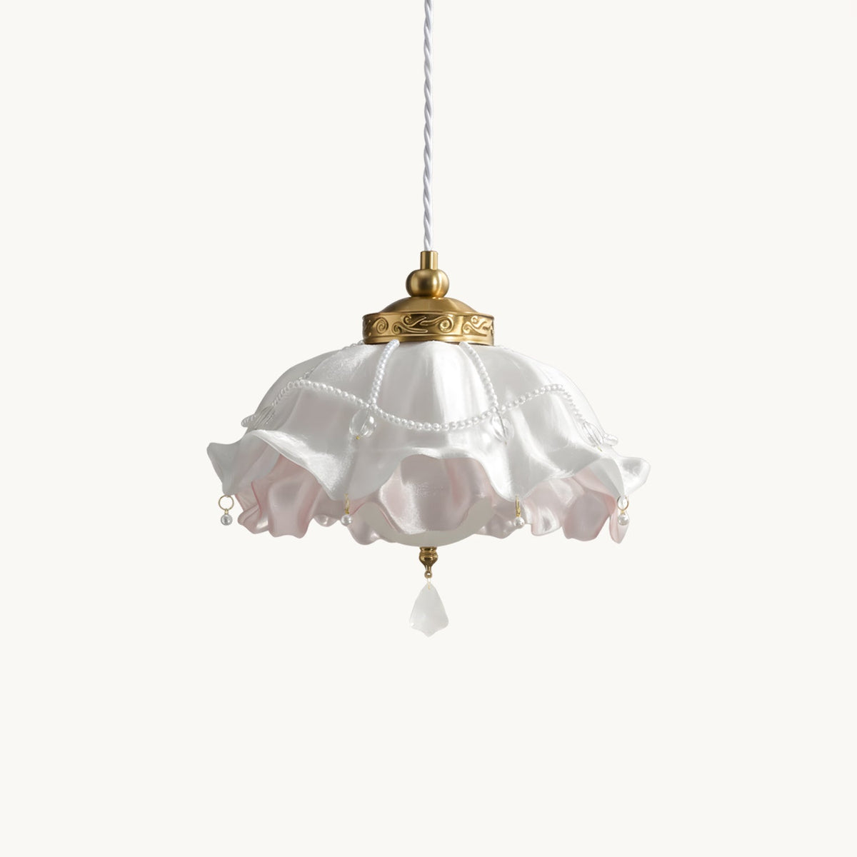 A Clérachic ruffled pendant light in white and pink on a plain off-white backdrop, with a brass cap, beaded trim and a crystal drop.