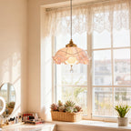 Lit Clérachic ruffled pendant glowing pink in front of a tall white window with a lace valance, above a dressing table and a basket of succulents.
