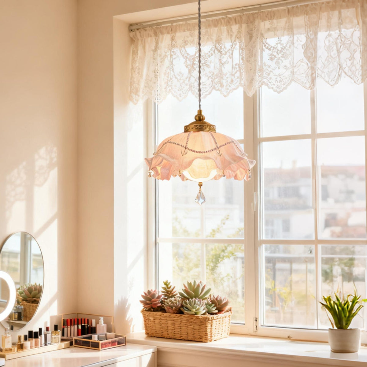 Lit Clérachic ruffled pendant glowing pink in front of a tall white window with a lace valance, above a dressing table and a basket of succulents.