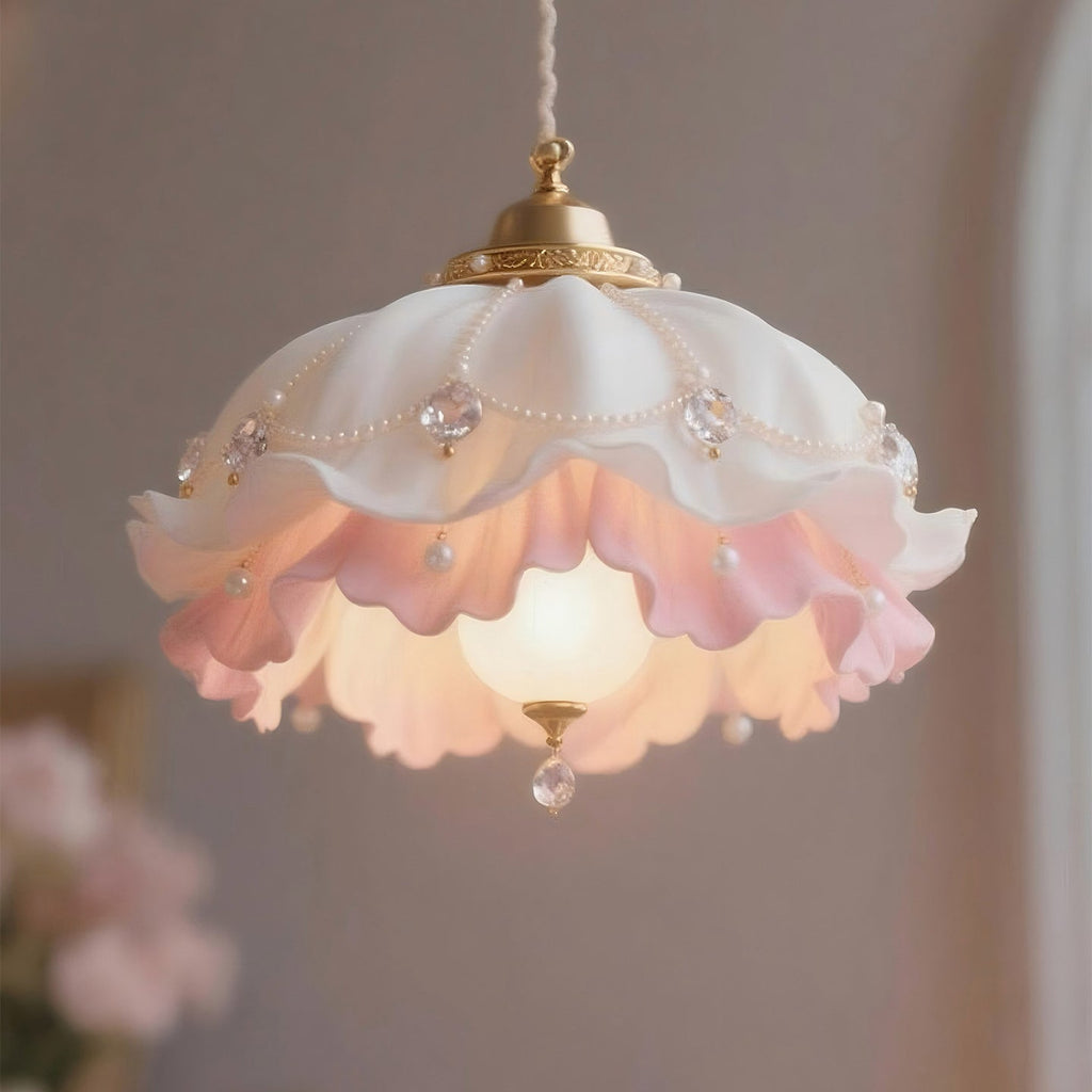 Close view of the white and pink ruffled shade on this Clérachic pendant, with pearl beads, small gems and a crystal drop under a glowing bulb.