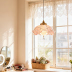Lit Clérachic pendant hanging in a bright window with a lace valance, a round mirror and a row of make-up on the sill below.