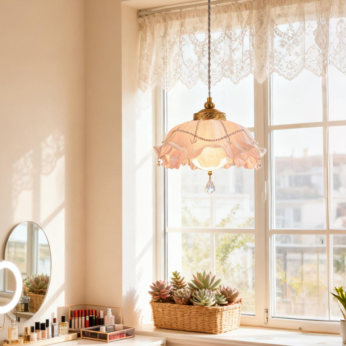 Lit Clérachic pendant hanging in a bright window with a lace valance, a round mirror and a row of make-up on the sill below.