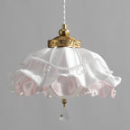 Unlit white and pink ruffled shade on this Clérachic pendant against a grey backdrop, with pearl strands, a brass collar and a crystal drop.