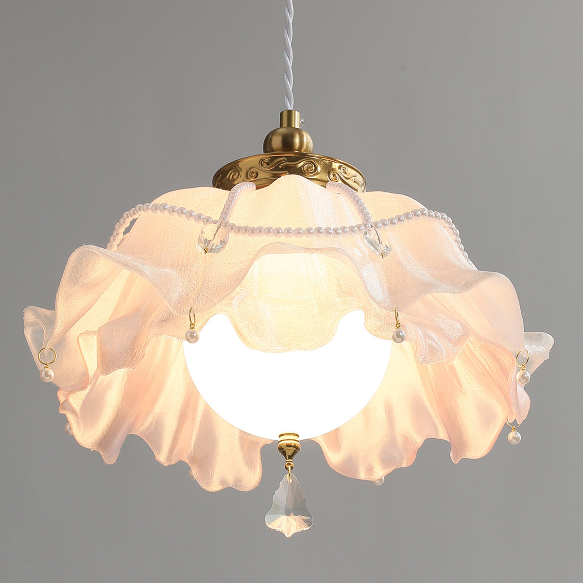Looking up into this Clérachic pendant: the frilled shade glows around a round bulb, with pearl beads and a faceted crystal drop below.