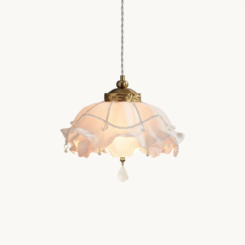 A lit Clérachic pendant with a ruffled pink-white shade and brass collar on a plain white backdrop, hanging from a twisted cord.