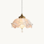 A lit Clérachic pendant with a ruffled pink-white shade and brass collar on a plain white backdrop, hanging from a twisted cord.