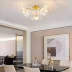 Three clear glass flowers on the Clérachic ceiling light hang over a mirrored console beside a dining table.