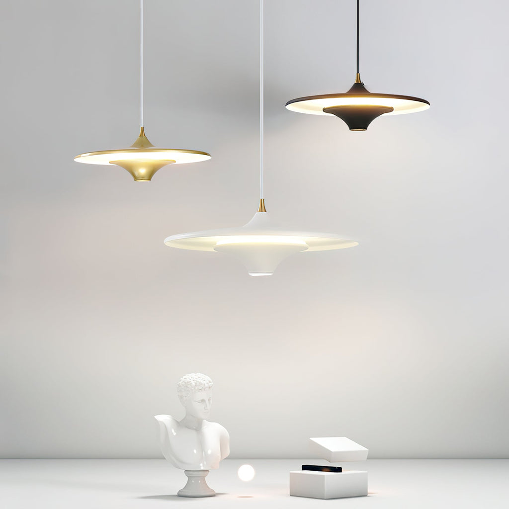 Three Clérachic saucer pendants in gold, black and white hang over a plaster bust and a small white box.
