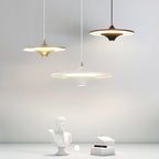 Three Clérachic saucer pendants in gold, black and white hang over a plaster bust and a small white box.