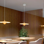 Two gold-toned Clérachic saucer pendants glow above a restaurant table set with plates, against slatted timber panelling.