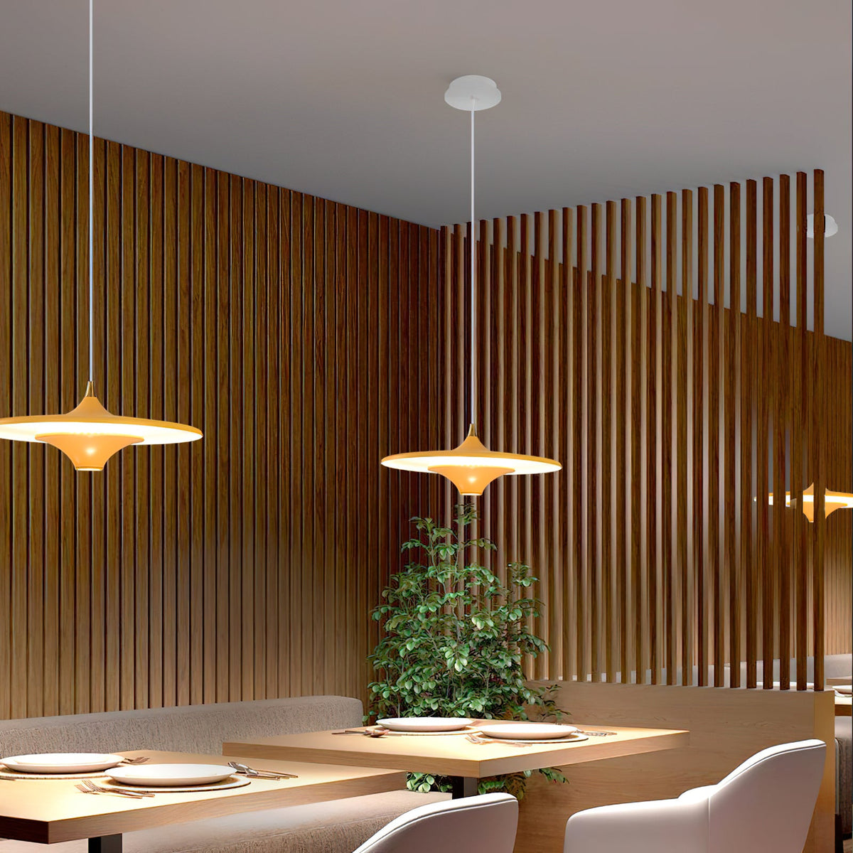 Two gold-toned Clérachic saucer pendants glow above a restaurant table set with plates, against slatted timber panelling.