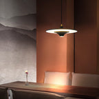 A black Clérachic saucer pendant lights a dark wood table in front of a rust-coloured wall with a mountain mural.