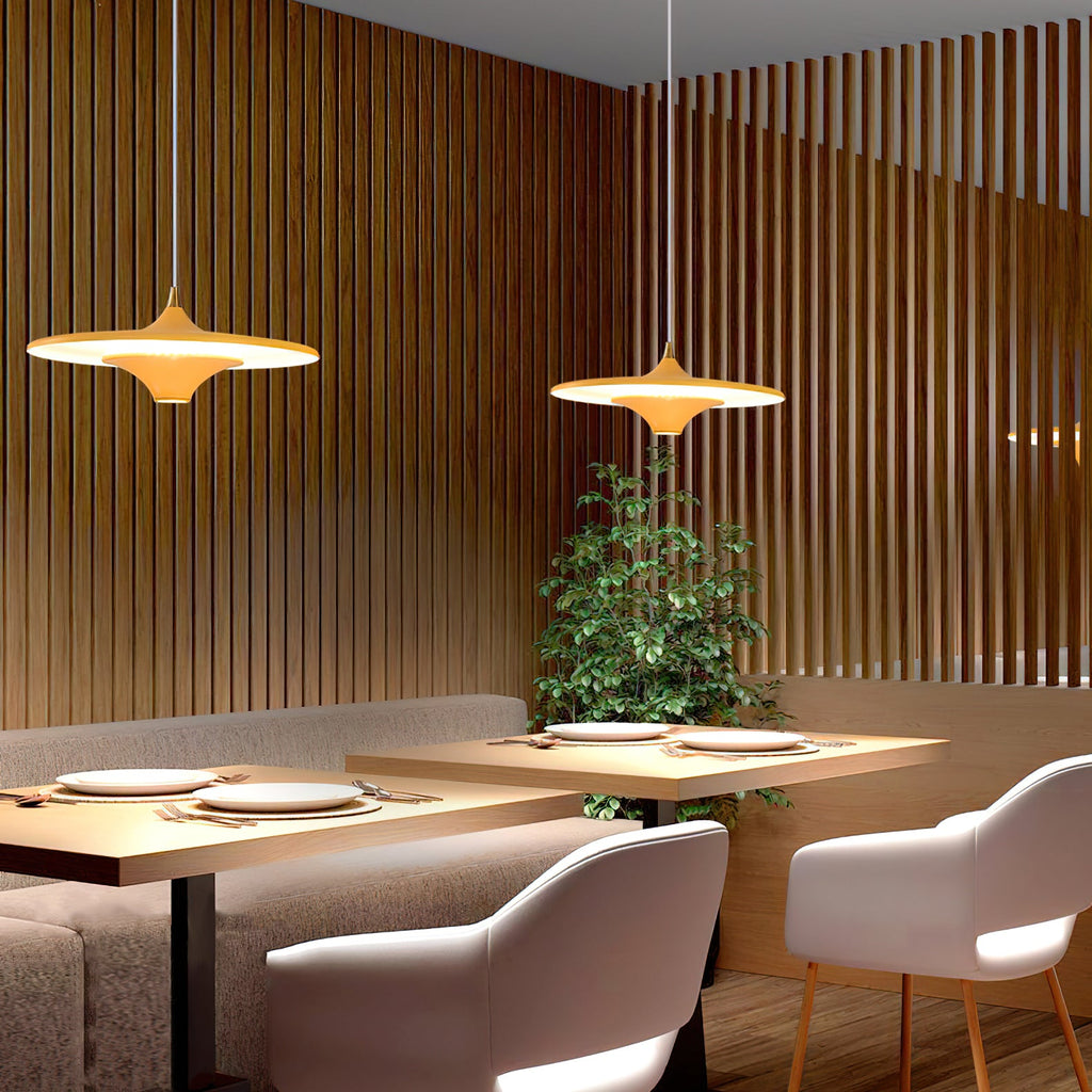 Pair of Clérachic saucer pendants with a warm glow over a restaurant booth, with a leafy plant behind the tables.