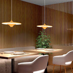 Pair of Clérachic saucer pendants with a warm glow over a restaurant booth, with a leafy plant behind the tables.