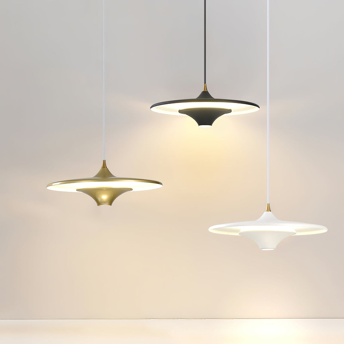 Gold, black and white Clérachic saucer pendants hang at different heights against a pale grey wall.