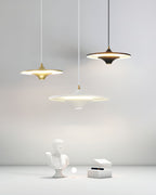 Three Clérachic saucer pendants in gold, black and white are lit above a plaster bust and white box in a light room.