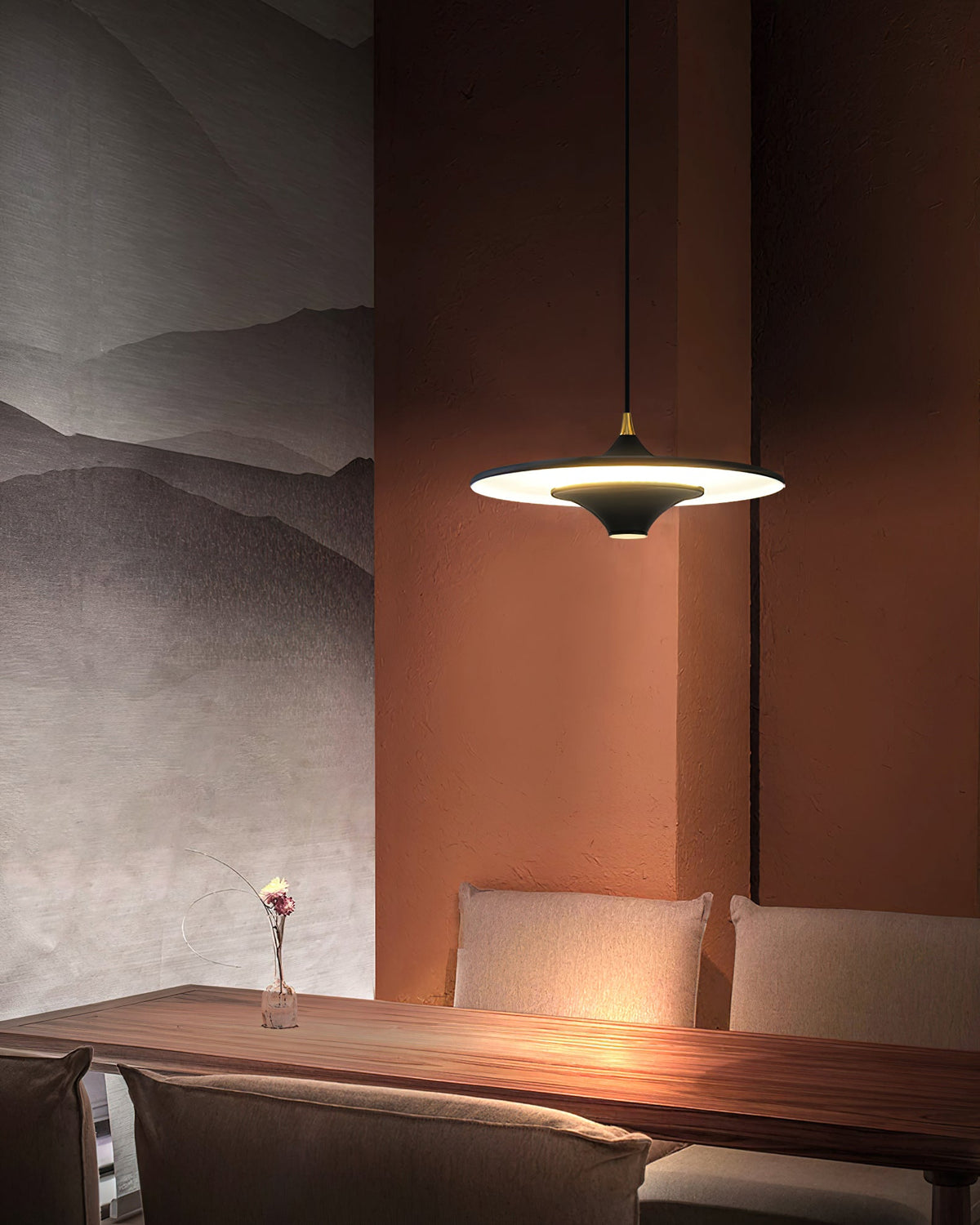 Black Clérachic saucer pendant glowing above a walnut table, set against a terracotta wall and grey mountain mural.