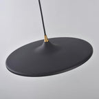 Underside view of the matt black disc on this Clérachic saucer pendant, with the brass collar and black cord above.