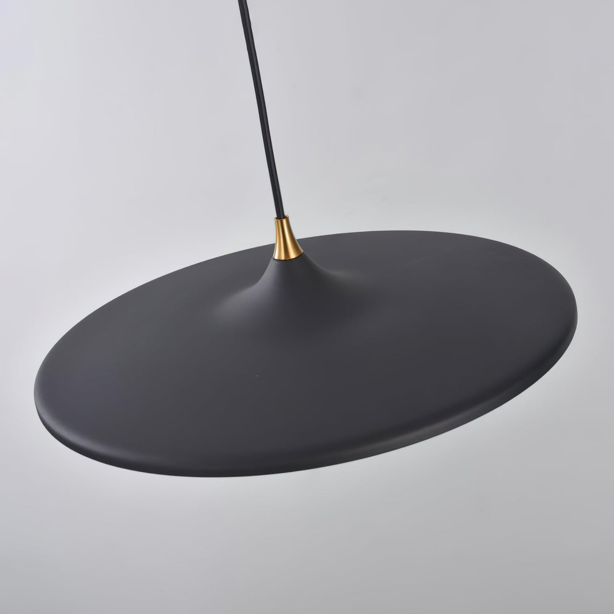 Underside view of the matt black disc on this Clérachic saucer pendant, with the brass collar and black cord above.
