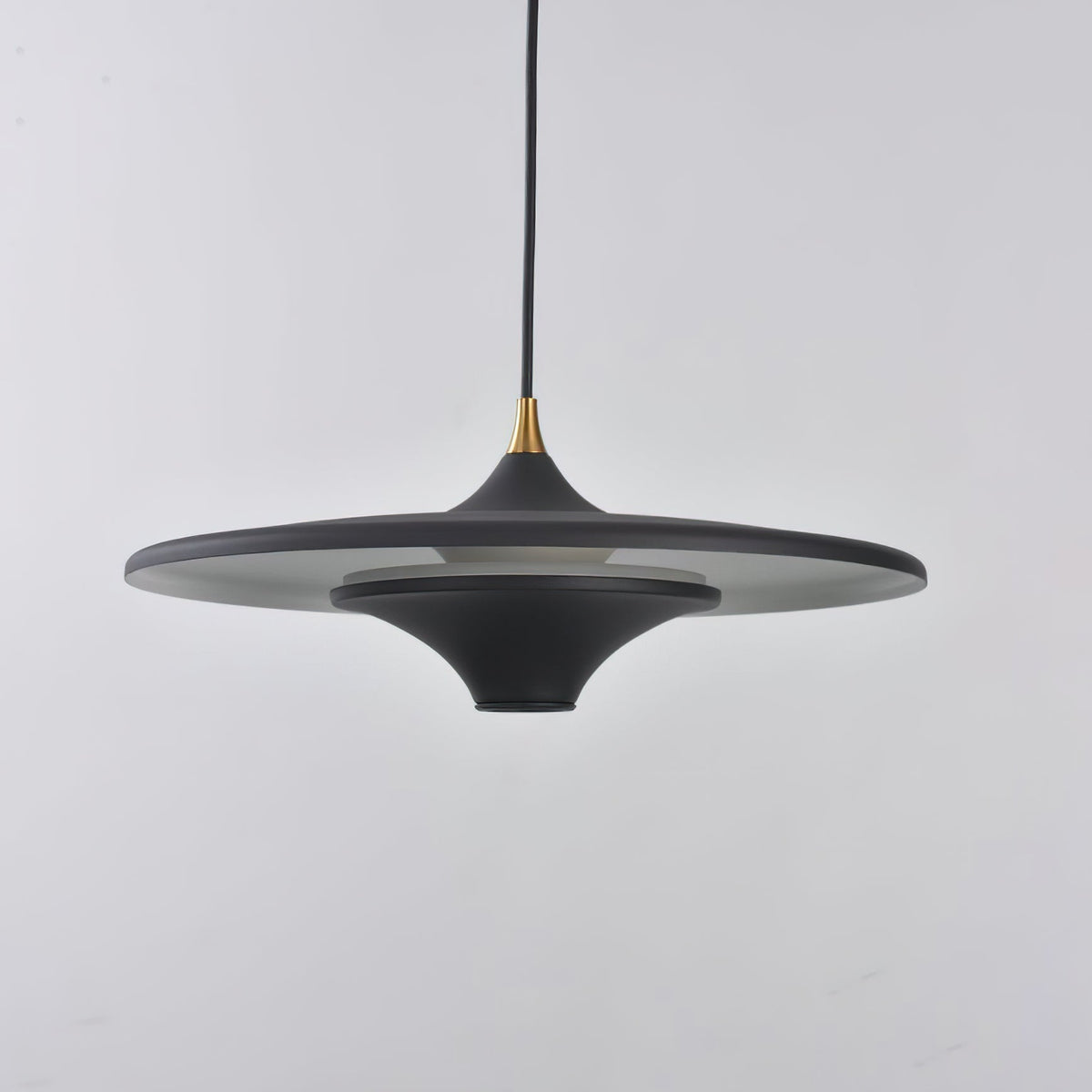 Matt black Clérachic saucer pendant with a brass collar, seen from the side against a light grey wall.