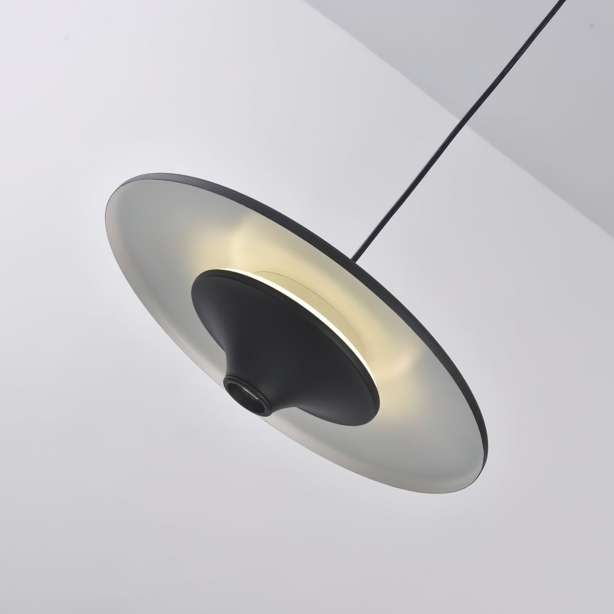 Tilted view of this Clérachic pendant lit, with a soft ring of light glowing around the black cone.
