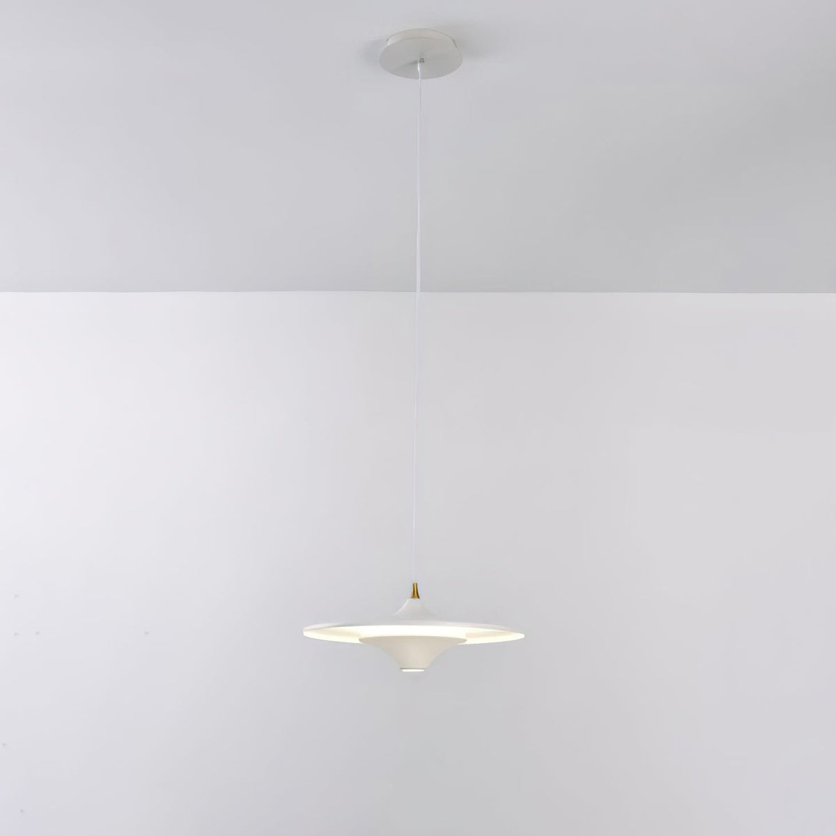 White Clérachic saucer pendant on a thin white cord from a white ceiling canopy, glowing softly against a grey wall.