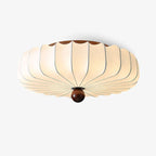 This Clérachic flush ceiling light on a plain backdrop, with a scalloped white fabric shade and a round walnut-colour wooden finial.
