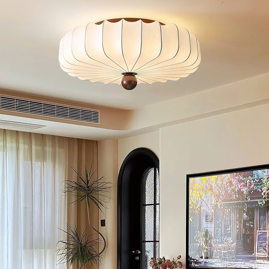 A Clérachic flush-mount light glowing on the ceiling of a bright living room with an arched black door and sheer curtains.