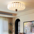 A Clérachic flush-mount light glowing on the ceiling of a bright living room with an arched black door and sheer curtains.