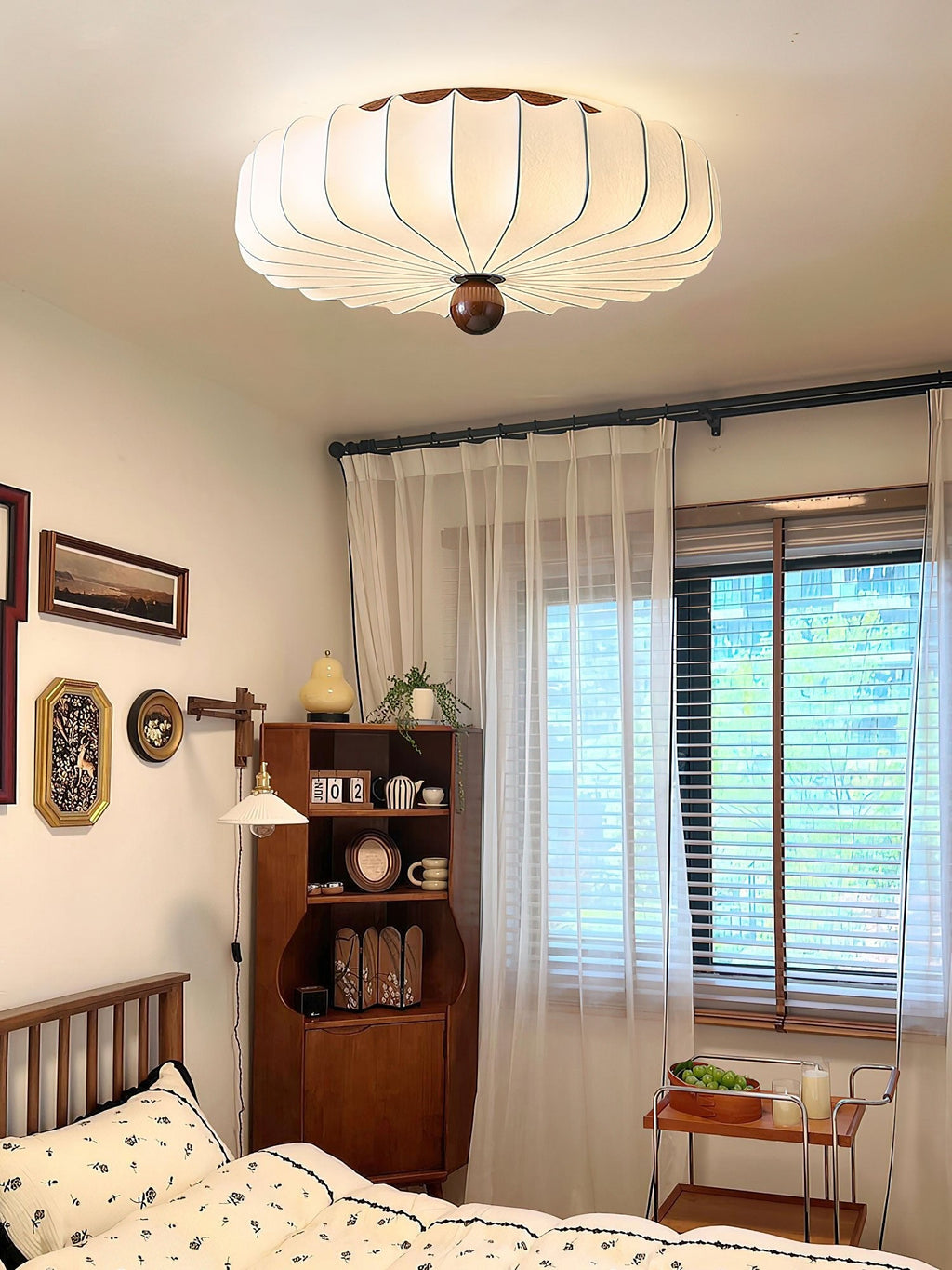 Ceiling-mounted Clérachic light with a ribbed white shade above a bedroom with a wooden shelf unit and sheer curtains at the window.