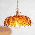 Clérachic Scalloped Flower Glass Pendant Light in amber glass, lit over a pale wall with its brass turn-knob collar in view.